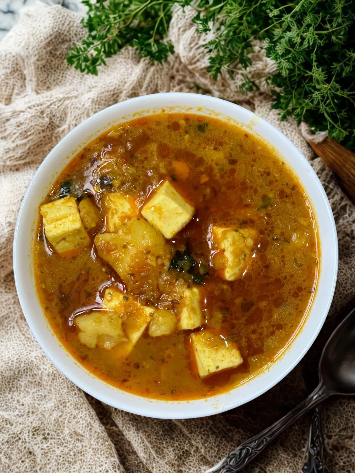 Golden paneer curry in a white bowl with cilantro garnish on linen, photographed from above