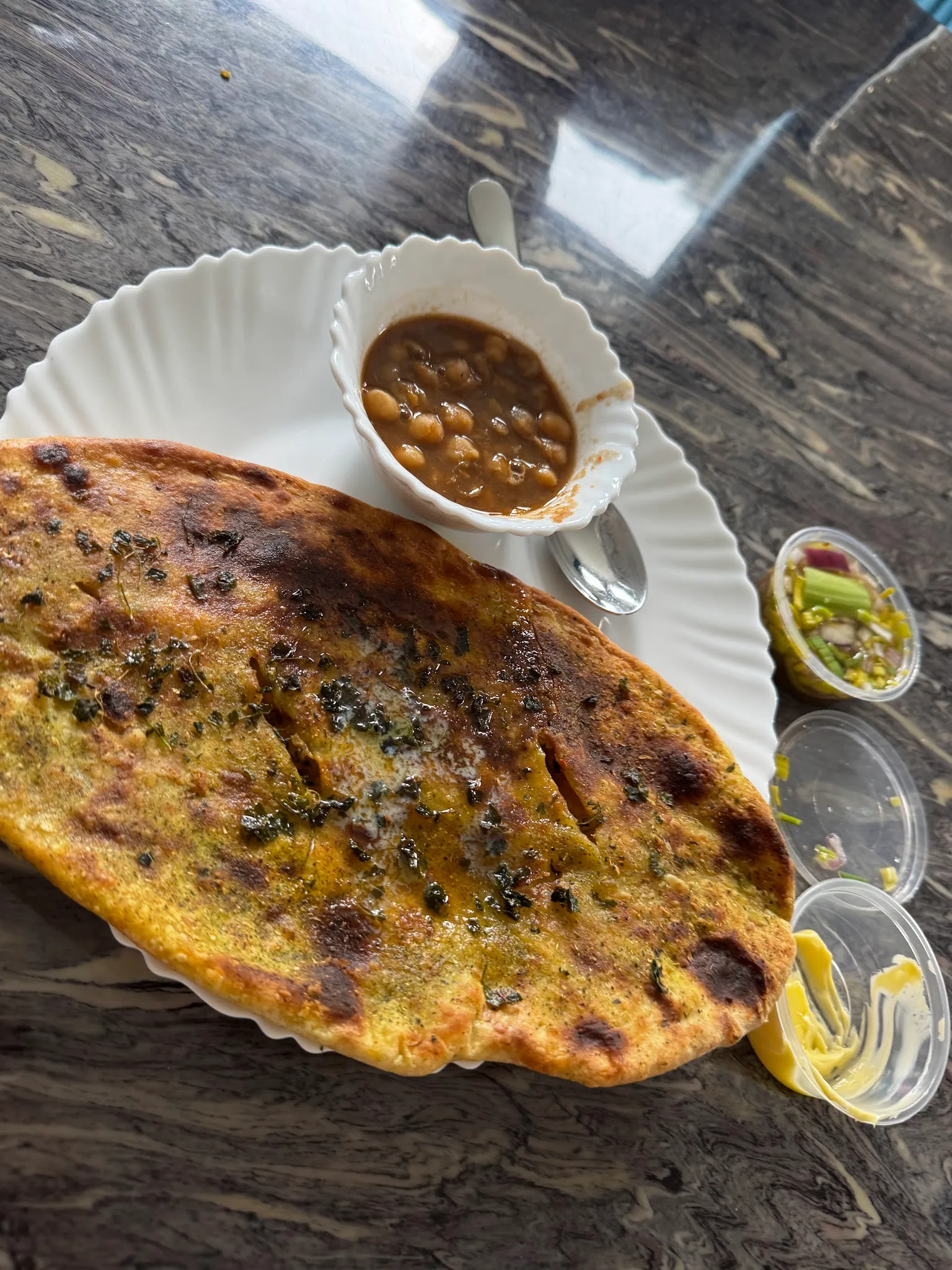 Charred aloo paratha on a paper plate with chana dal and condiments