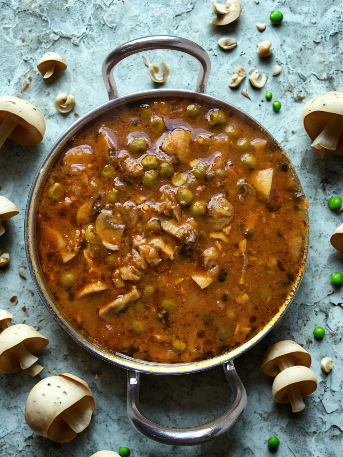 Matar mushroom curry in a grey kadhai on stone with scattered raw mushrooms, peas, and cashews